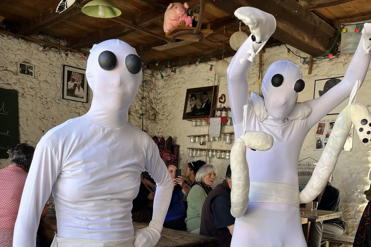 Deux personnes en combinaison blanche et masque d’alien, dans la salle du Café